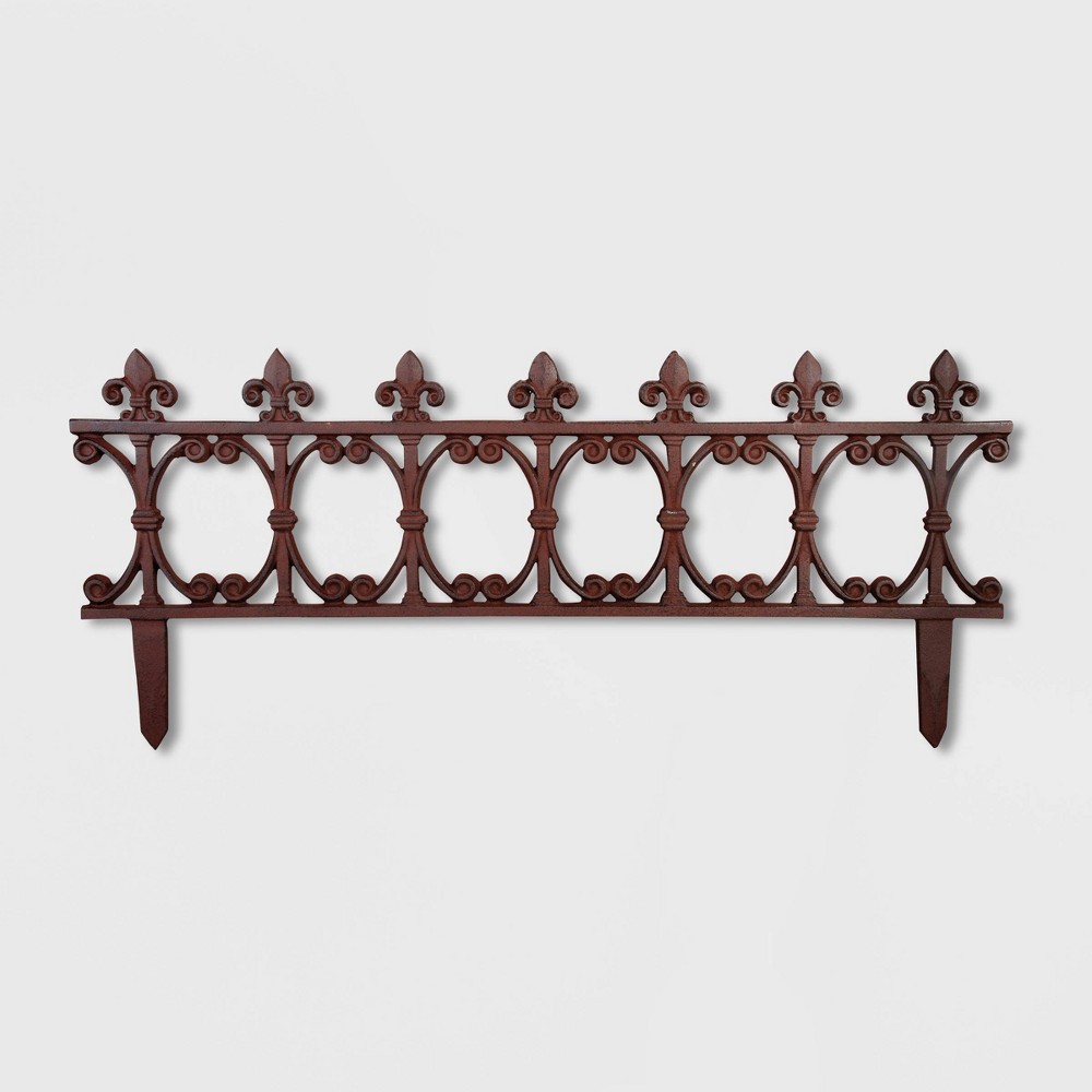 Rustic cast iron garden fence in a dark brown finish, featuring decorative fleur-de-lis motifs and six panels with pointed tops, designed for easy installation with stakes.