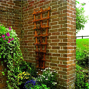 Wooden decorative fan wall trellis in a warm brown finish, measuring 2' x 6', mounted on a brick wall, surrounded by vibrant flowers and lush greenery.