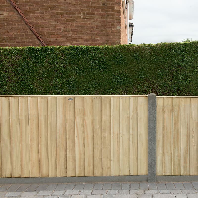 Pressure treated vertical closeboard fence panel in natural wood color, measuring 6' x 3', with a smooth finish and concrete posts, set against a green hedge backdrop.