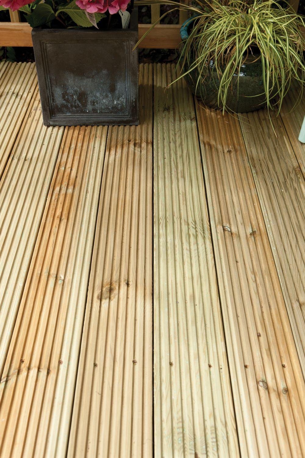 Light-colored, treated softwood deck boards arranged on a wooden surface, showcasing their smooth texture and natural grain, with a potted plant and decorative item nearby.