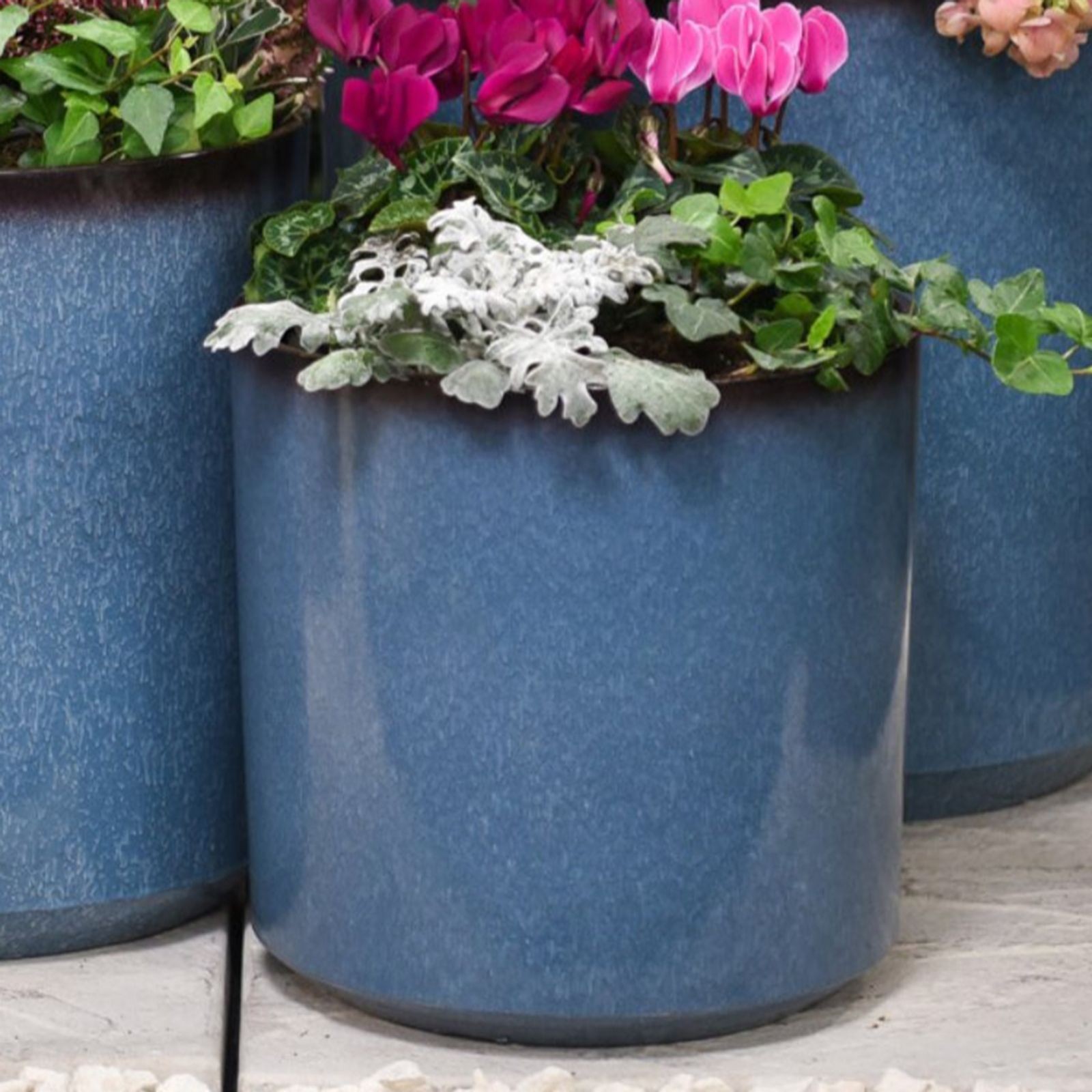 Glazed 26cm blue ceramic planter with a smooth finish, featuring vibrant pink flowers and lush green foliage, set on a light stone surface.