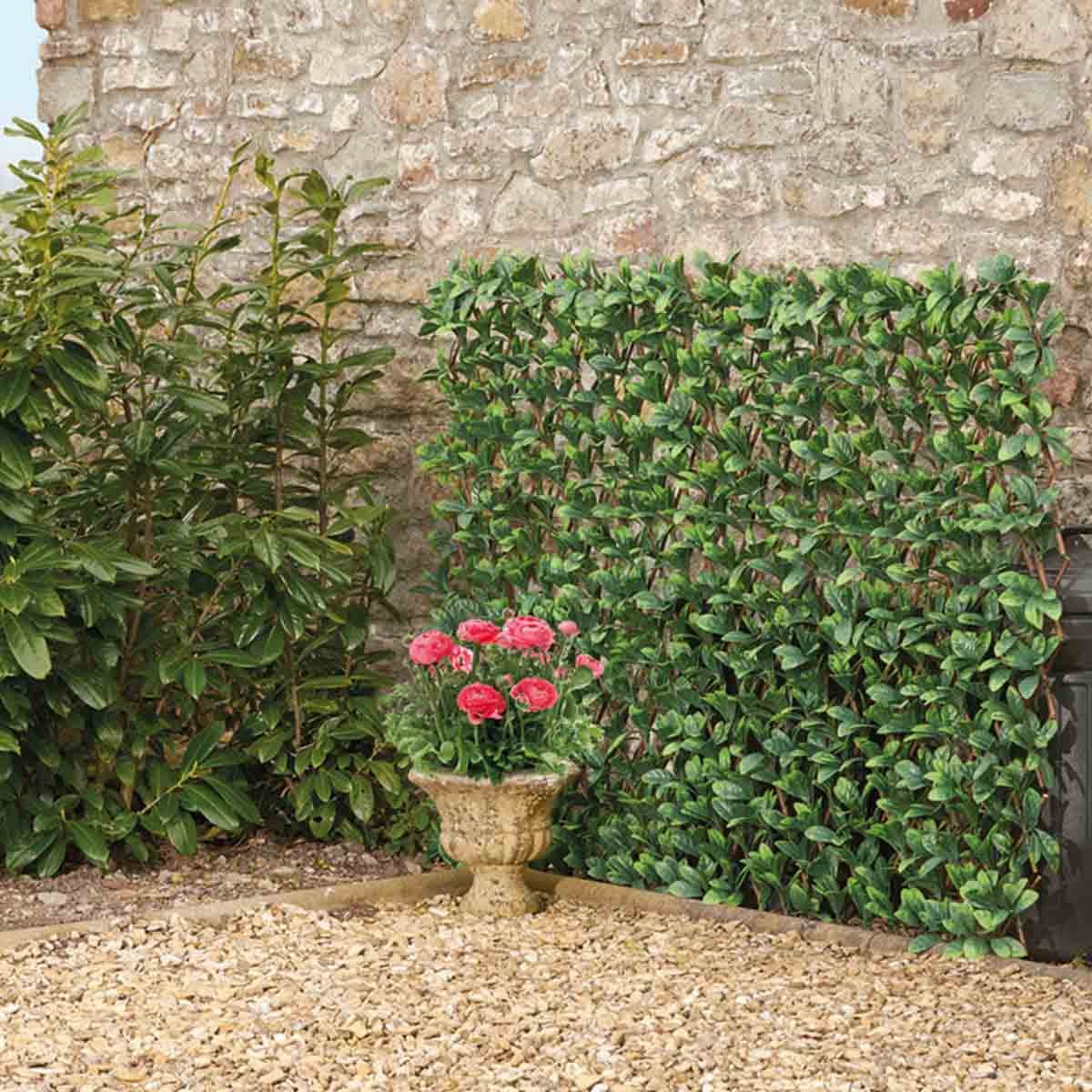 Laurel leaf folding hedge trellis in green, measuring 1x2m, features a realistic leaf design, ideal for garden decoration or privacy, set against a stone wall with potted flowers nearby.