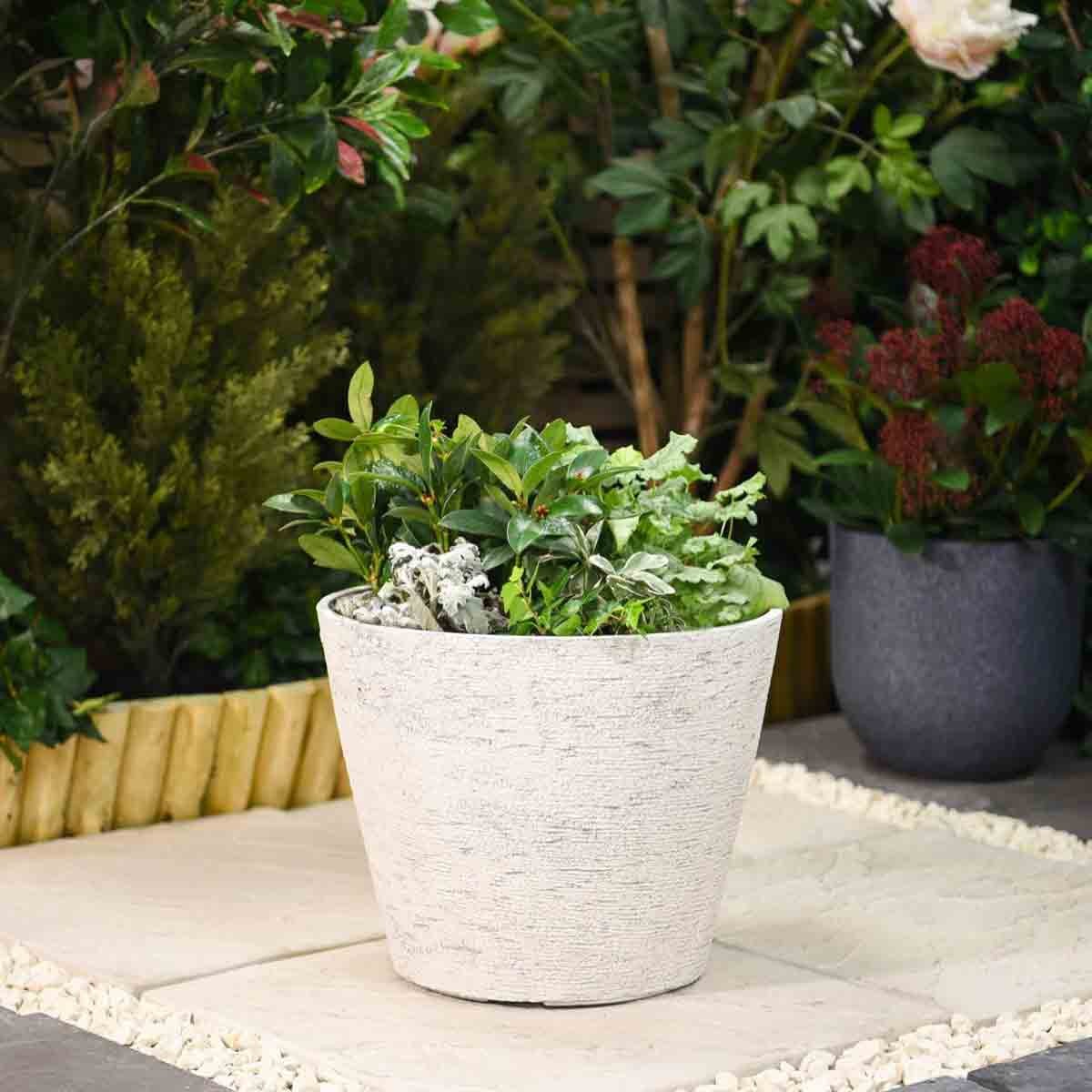 Stone effect white planter with a textured grey finish, measuring 36.5 cm, filled with lush green plants, set against a garden backdrop.