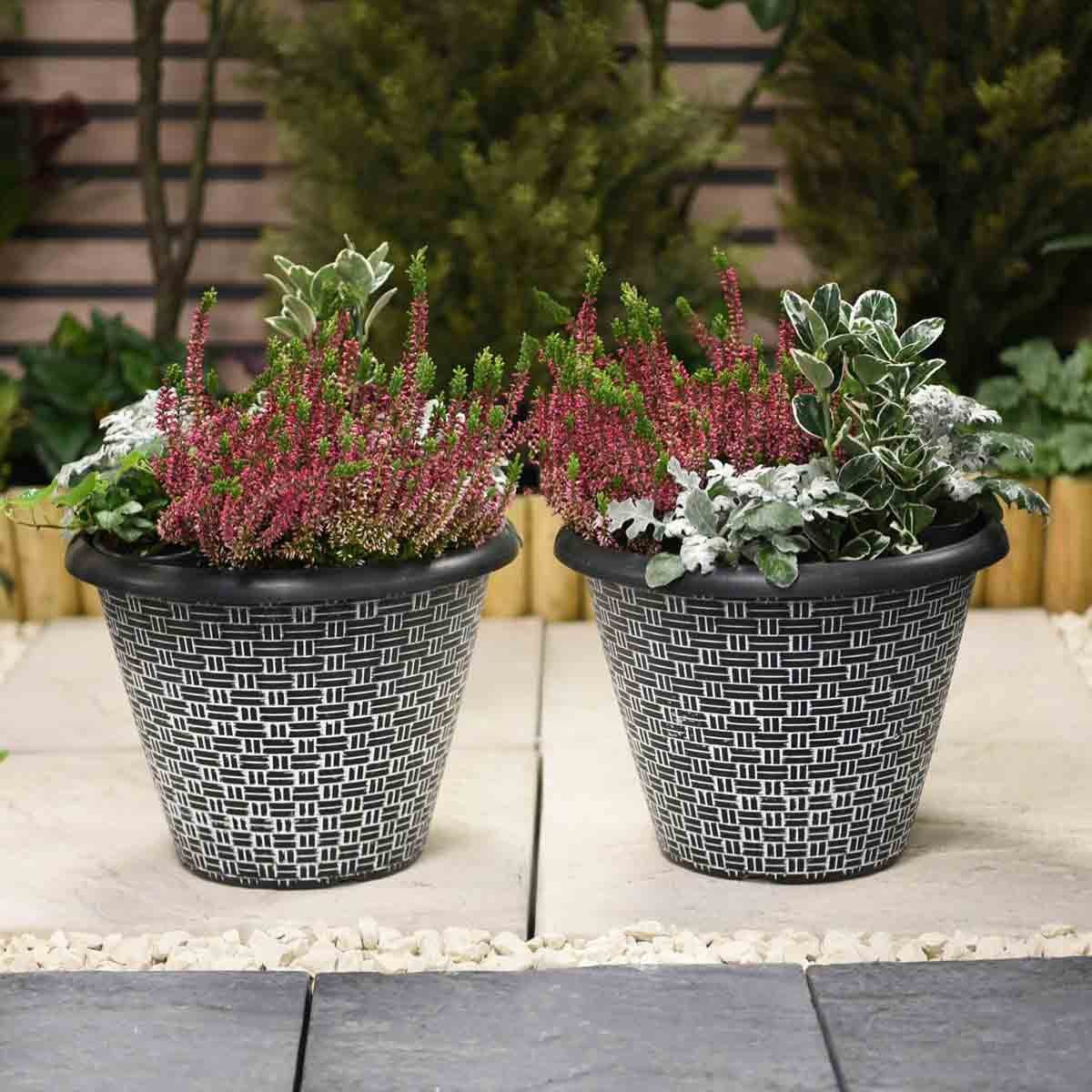 Two grey, weave effect planters, 30.5 cm in diameter, filled with vibrant pink and green plants, set against a garden backdrop with stone and gravel.