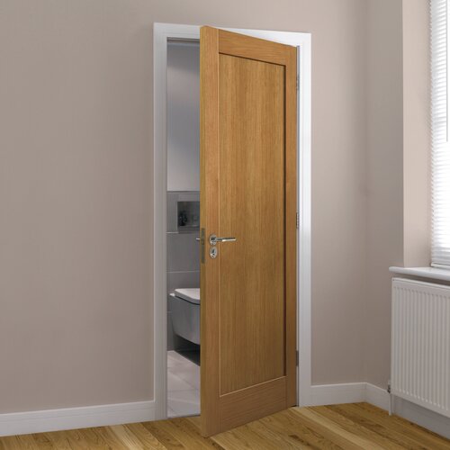 Unfinished oak internal fire door with a simple design, featuring a single panel and silver handle, set against a light-colored wall and visible bathroom in the background.