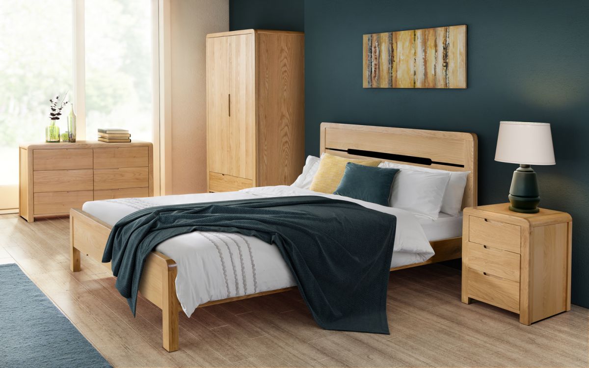 Curved oak chest of three drawers with a natural wood finish, featuring sleek lines and a minimalist design, complements a modern bedroom setting with a dark green wall.
