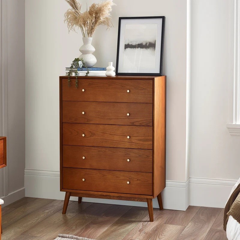 Lowry 5 Drawer Chest in dark wood featuring a sleek design, five spacious drawers with round gold knobs, and tapered legs, complemented by decorative elements on top.