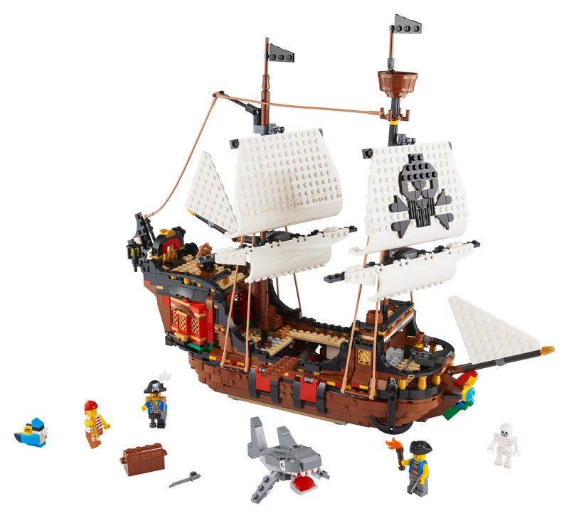 Colorful LEGO Creator 3 in 1 Pirate Ship set featuring a brown ship with white sails, pirate minifigures, a treasure chest, and a shark, all set on a white background.