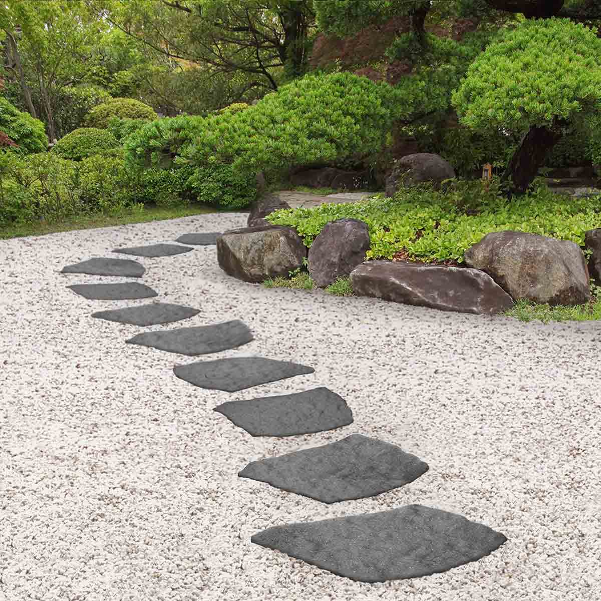 Four grey natural stepping stones arranged along a gravel path in a garden, featuring a textured surface and a rectangular shape, surrounded by greenery and rocks.
