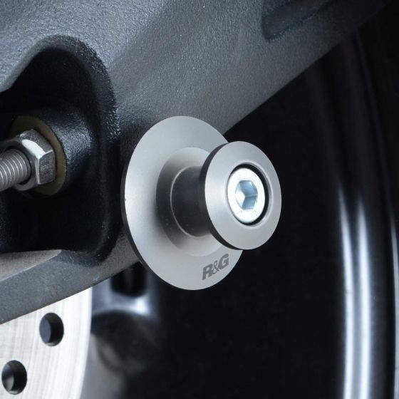Titanium grey R&G M8 elevation paddock stand bobbin featuring a circular design with a hexagonal bolt and branded logo, mounted on a motorcycle's swingarm.