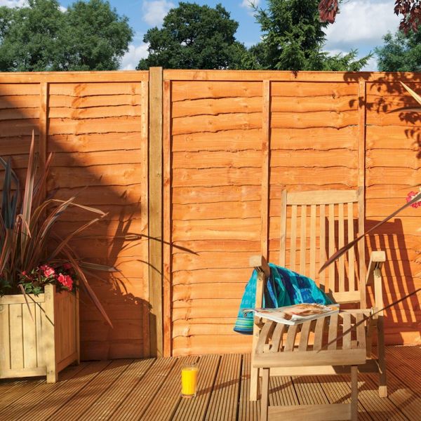 Rowlinson Lap Panels in a warm, dipped wood finish, featuring a sturdy design with horizontal slats, set against a garden backdrop with greenery and a wooden chair.