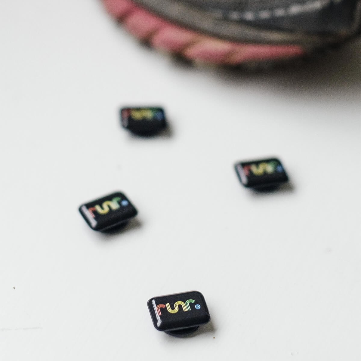 Colorful RUNR race magnets in a rectangular shape, featuring a vibrant logo, set against a white background near a running shoe.