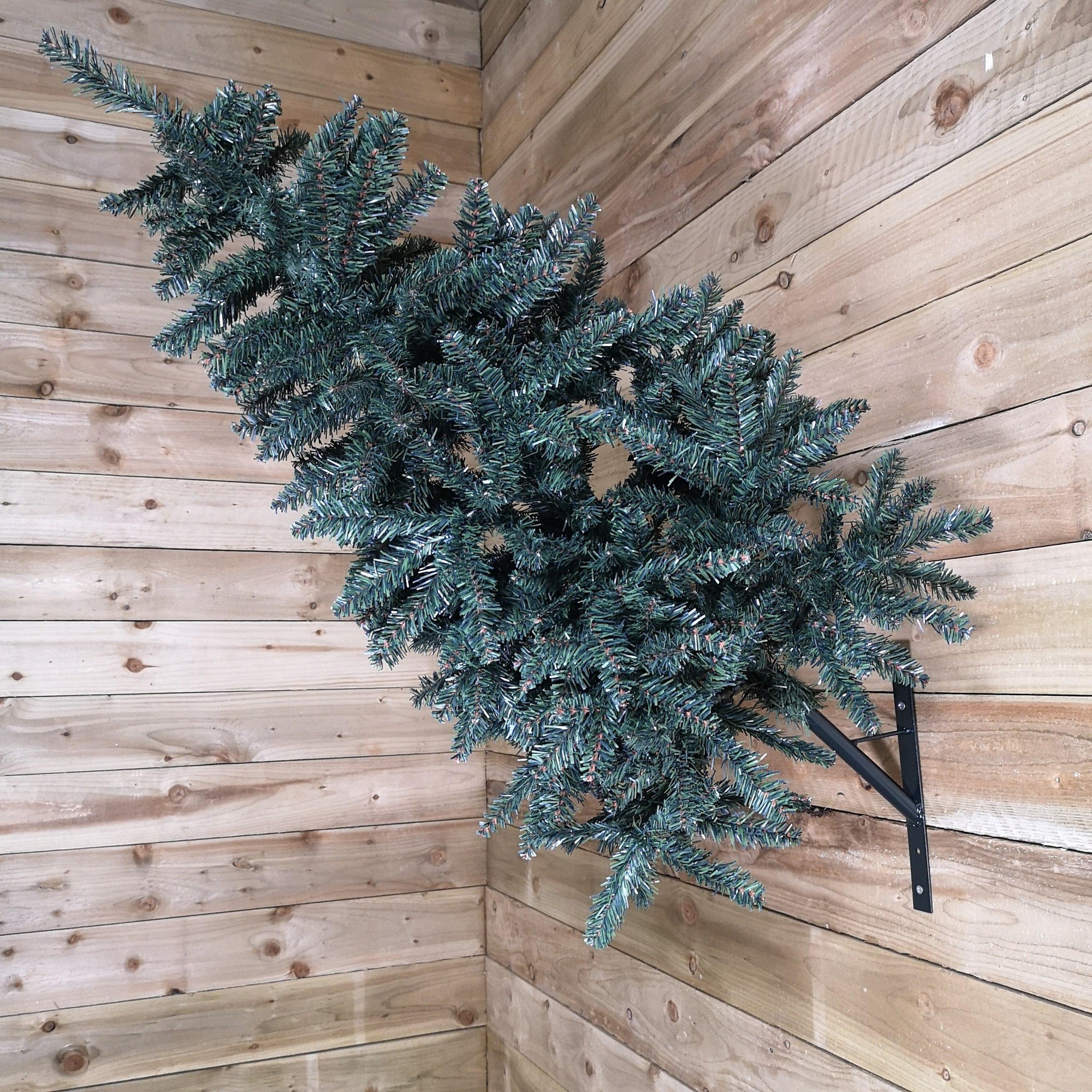 90cm green PVC indoor wall-mounted Christmas tree with wrapped branches, secured by a black metal bracket, positioned against a wooden wall.