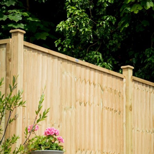 Closeboard fence panel in natural wood finish, standing 0.9m tall, featuring vertical slats and decorative top posts, set against a lush green backdrop with pink flowers nearby.