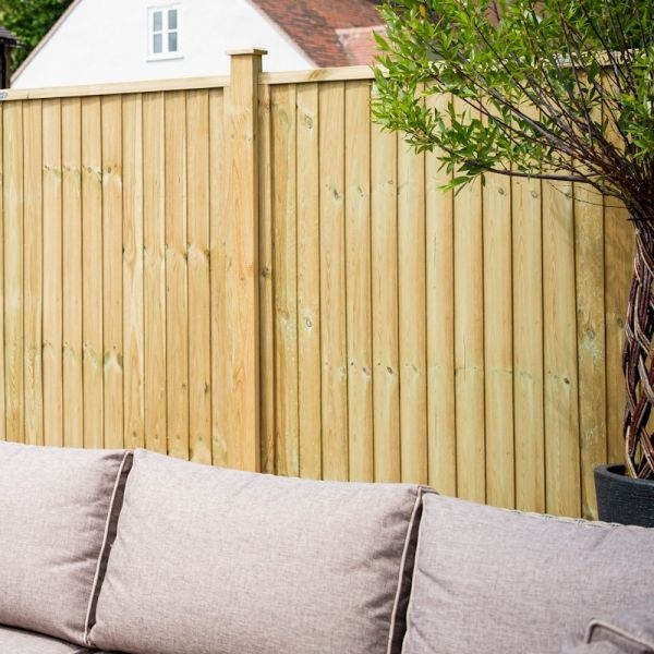 Green treated wooden closeboard panel fence, 1.5m high, featuring vertical slats and a smooth finish, set against a backdrop of a garden with a potted plant and outdoor seating.