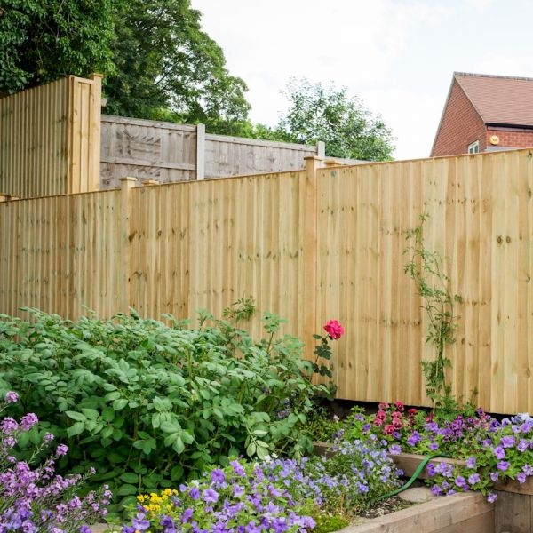 Grange Standard Featheredge Panel in green, measuring 1.2m, features vertical timber boards with a smooth finish, surrounded by vibrant garden flowers and greenery.
