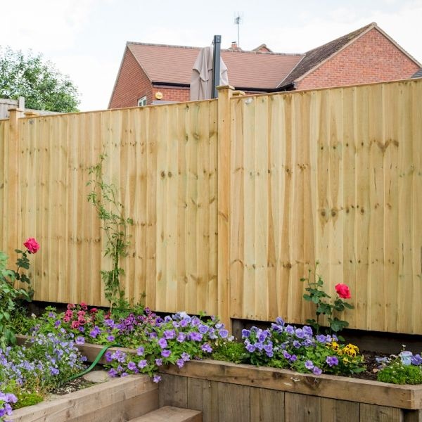 Grange Featheredge fence panel in natural wood finish, measuring 6ft x 5ft, featuring vertical boards, topped with a smooth edge, surrounded by colorful flowers in a garden setting.