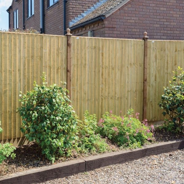 Featheredge wooden fence panel in natural wood finish, 1.8m high, with vertical slats and sturdy brown posts, surrounded by green shrubs and gravel pathway.