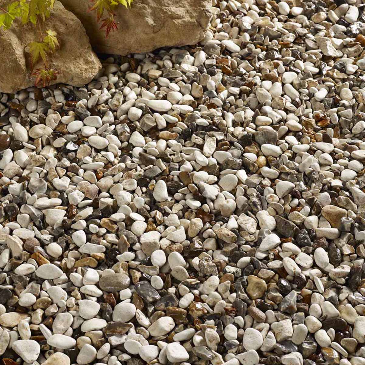Cottage cream decorative aggregate in a bulk bag, featuring smooth, rounded pebbles in shades of cream, brown, and gray, scattered among natural stone elements.