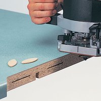 Router cutting slot in wood with Trend Slotter 11mm kerf, M12mm bore, visible biscuit joints on green laminate surface.