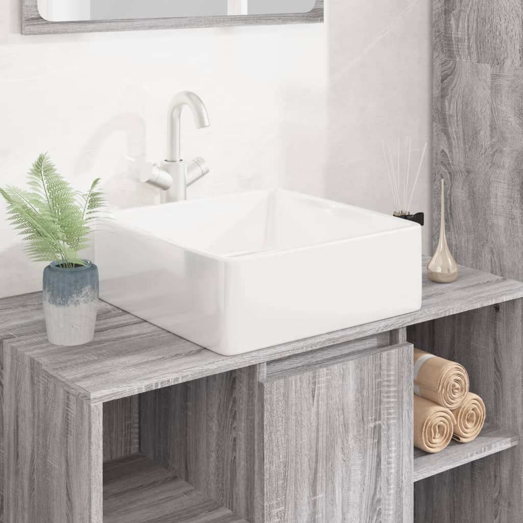 White ceramic square wash basin measuring 37x37x13 cm, featuring a sleek design, placed on a wooden countertop with a plant and rolled towels nearby.