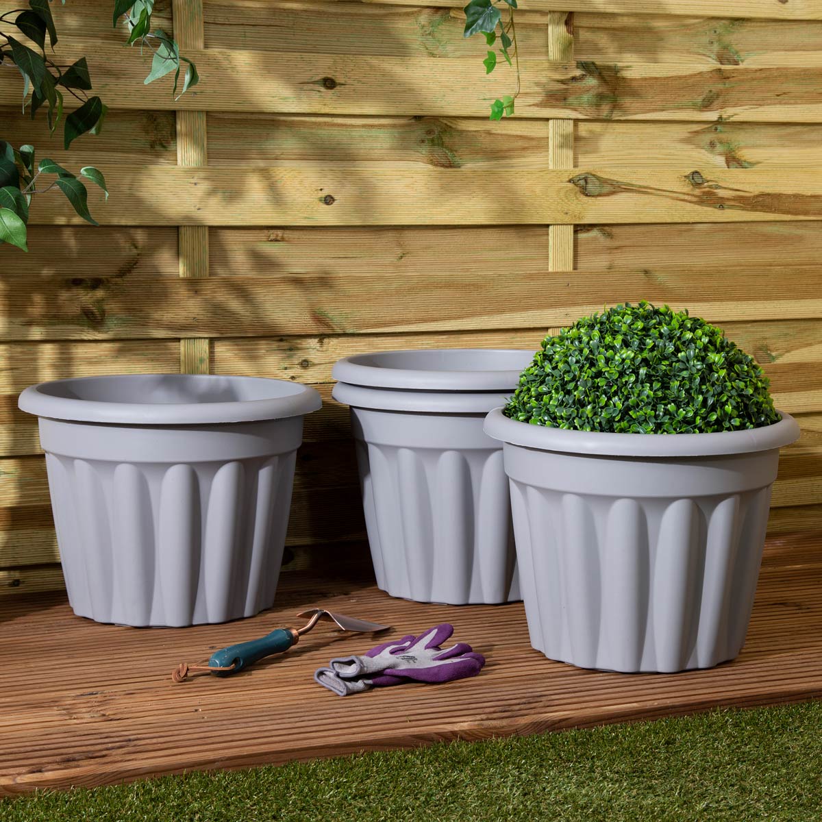 Set of four 40cm round grey planters with ribbed design, made from durable material, placed on a wooden surface with gardening gloves and tools nearby.