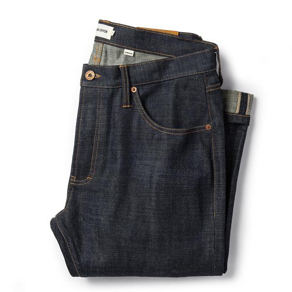 Dark blue organic selvage denim jeans featuring a classic five-pocket design, contrast stitching, and a folded cuff.