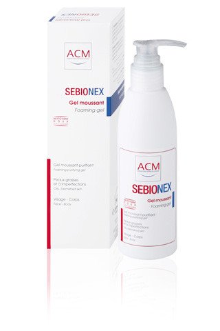 White plastic bottle with a pump dispenser, labeled "SEBIONEX" in red and blue, alongside a matching white box, both designed for cleansing problematic skin.