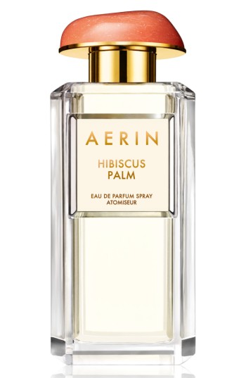 Clear glass bottle with a gold label reading "AERIN HIBISCUS PALM," topped with a coral-colored cap, containing a light yellow perfume.