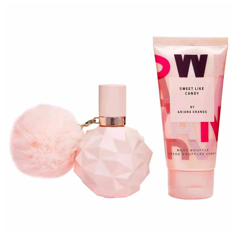 A pink geometric perfume bottle with a fluffy pom-pom cap alongside a pink and white tube of body souffle, both labeled "Sweet Like Candy" by Ariana Grande.