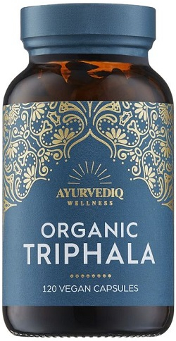Dark amber glass bottle with a blue label featuring gold intricate patterns, labeled "AYURVEDIQ WELLNESS ORGANIC TRIPHALA - 120 VEGAN CAPSULES."