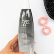 Debenhams Dream Shine Spray in a sleek, translucent gray bottle with a black cap, featuring the Beauty Works logo, alongside pink hair ties and a black hairbrush.