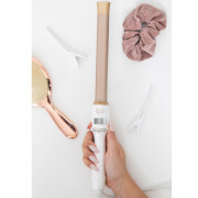 Beauty Works Flat Iron Curl Bar in 25mm features a sleek white body, a smooth beige barrel, and a digital temperature display, accompanied by a pink scrunchie and hair clips.