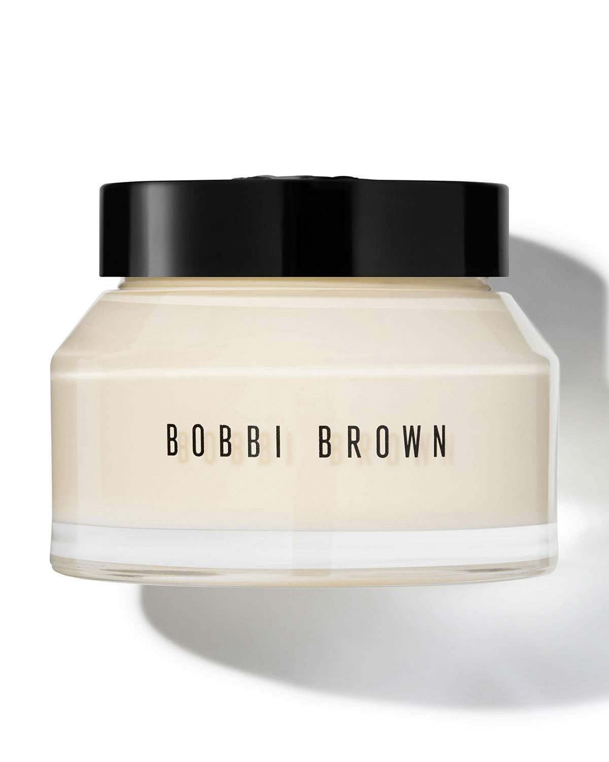 Bobbi Brown Deluxe Vitamin Enriched Face Base in a clear jar with a black lid, showcasing a creamy, off-white moisturizer inside.