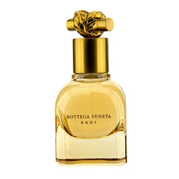 Clear glass perfume bottle with a rounded base, featuring a gold cap adorned with a knotted design, labeled "Bottega Veneta Knot" in elegant font, filled with light golden fragrance.
