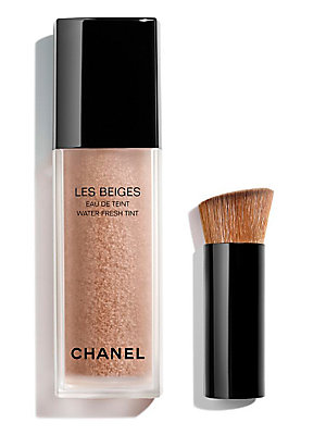 Chanel Les Beiges Water-Fresh Tint in a clear glass bottle with a black cap, featuring a light beige liquid and a small brush with a wooden handle.