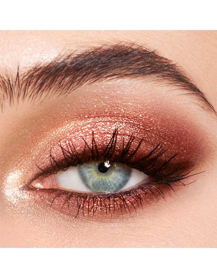 Close-up of an eye showcasing shimmering eyeshadow in warm pink and copper tones, with voluminous lashes and a soft, blended finish.