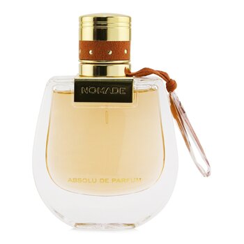 Clear glass perfume bottle with a rounded shape, featuring a gold cap and a brown leather strap, labeled "NOMADE" in gold, containing a light amber liquid.