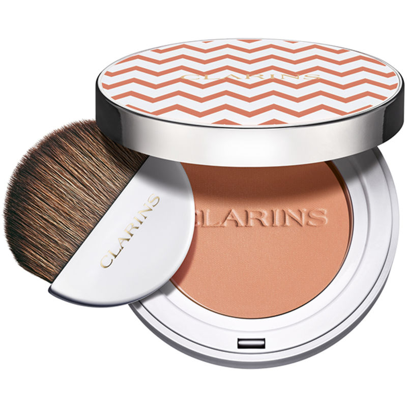 Round compact featuring a peachy blush with a chevron-patterned lid, accompanied by a soft brush for application, all in a sleek white case.