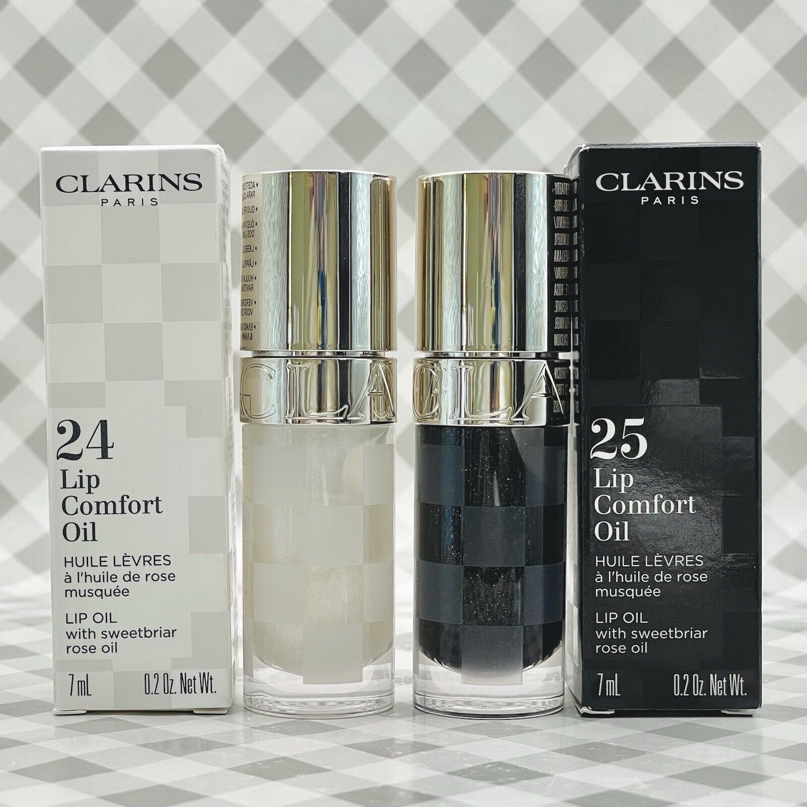 Clarins Lip Comfort Oil in shade 24 White, featuring a sleek clear bottle with a silver cap, alongside a black variant, both in elegant packaging.