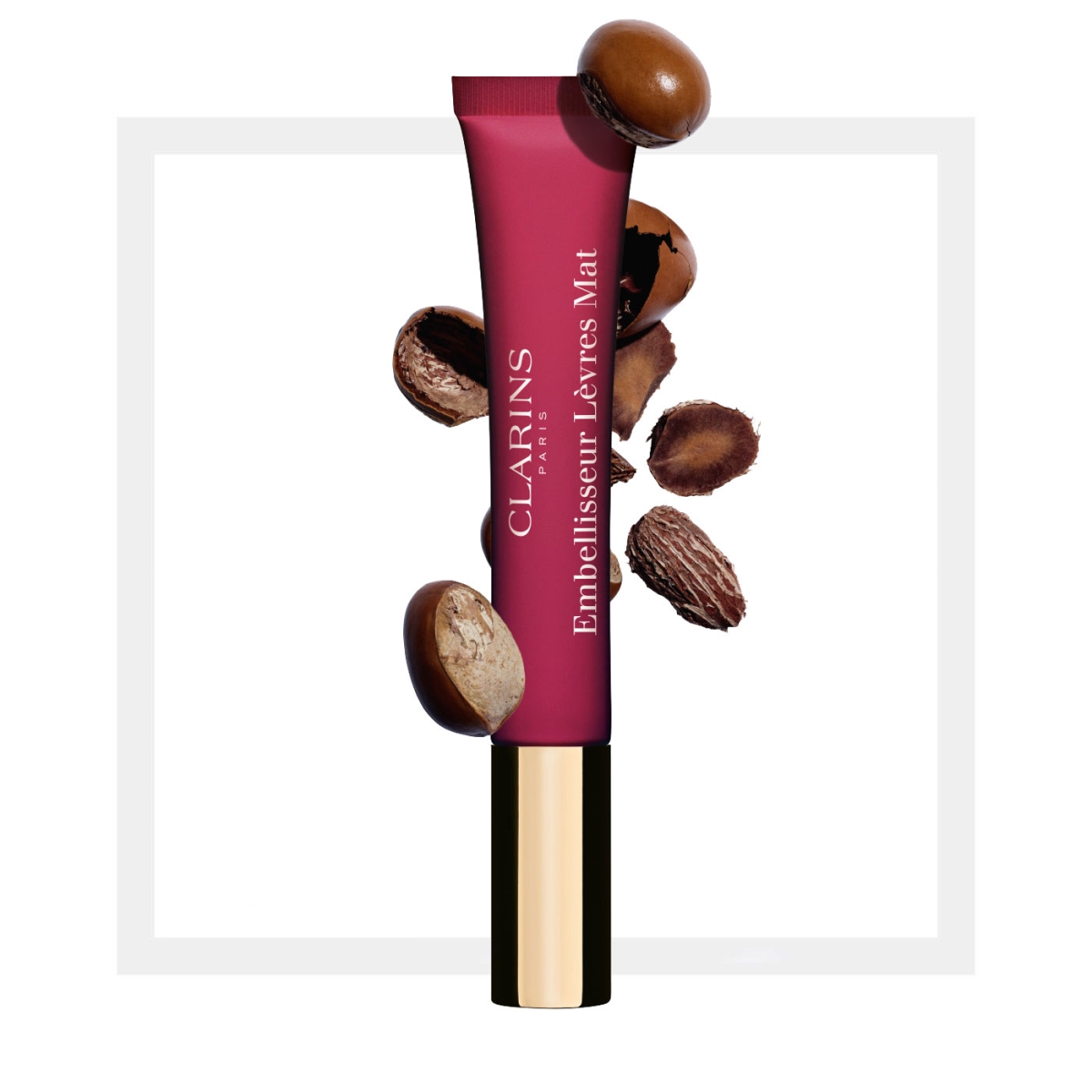 Clarins Velvet Lip Perfector in a pink tube with a gold base, featuring a matte finish and surrounded by cocoa beans, highlighting its luxurious and nourishing qualities.