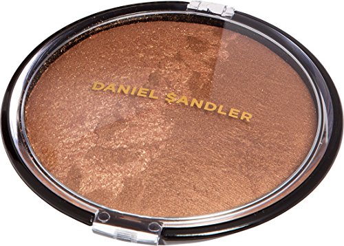 Round compact of Daniel Sandler's Billion Dollar Body Shimmer, featuring a shimmering bronze powder inside, with a clear lid and gold lettering on a black base.
