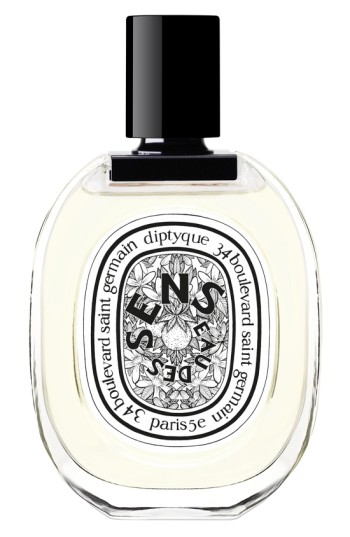 Clear glass bottle with a rounded shape, featuring a black cap and a decorative label with "Eau Des Sens" in elegant typography, containing a light yellow fragrance.