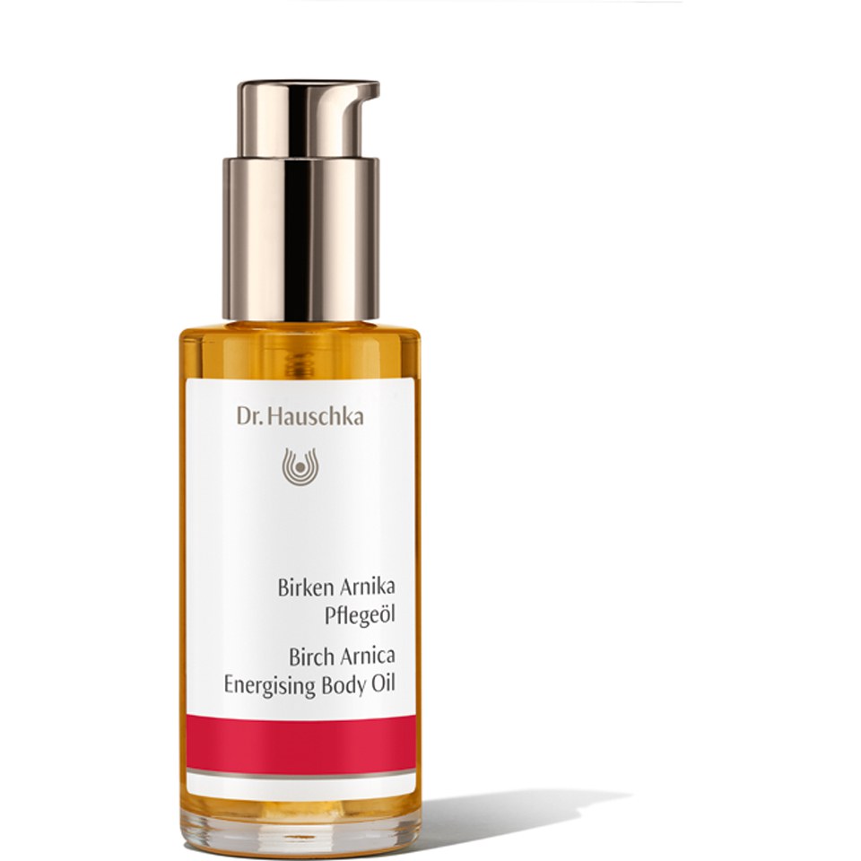 Amber-colored body oil in a sleek glass bottle with a pump dispenser, featuring a white and red label that reads "Birch Arnica Energising Body Oil" by Dr. Hauschka.