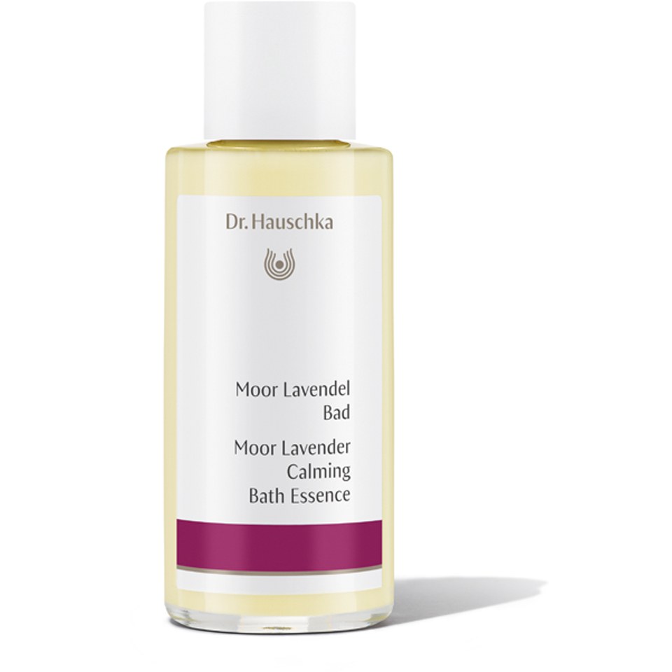 Clear glass bottle with a white cap, containing a pale yellow liquid labeled "Moor Lavender Calming Bath Essence" by Dr. Hauschka, featuring a purple accent at the bottom.