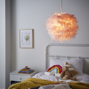 A 40cm pink feather light shade hangs above a white bed with colorful blankets and pillows, accompanied by a bedside table with books and a framed bee illustration.