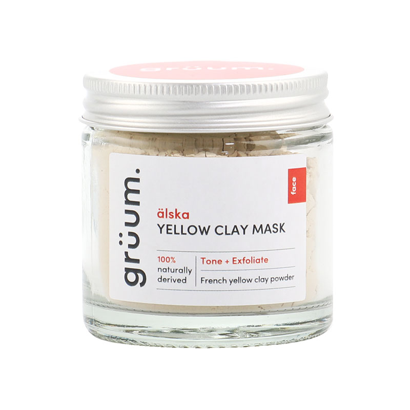 Glass jar with a silver lid containing yellow clay face mask, labeled "grüum alska Yellow Clay Mask," highlighting its natural ingredients and exfoliating properties.