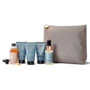 Five hair care products in a soft taupe pouch, including a bottle of serum, two tubes of shampoo, and two tubes of conditioner, all featuring elegant, minimalist packaging.
