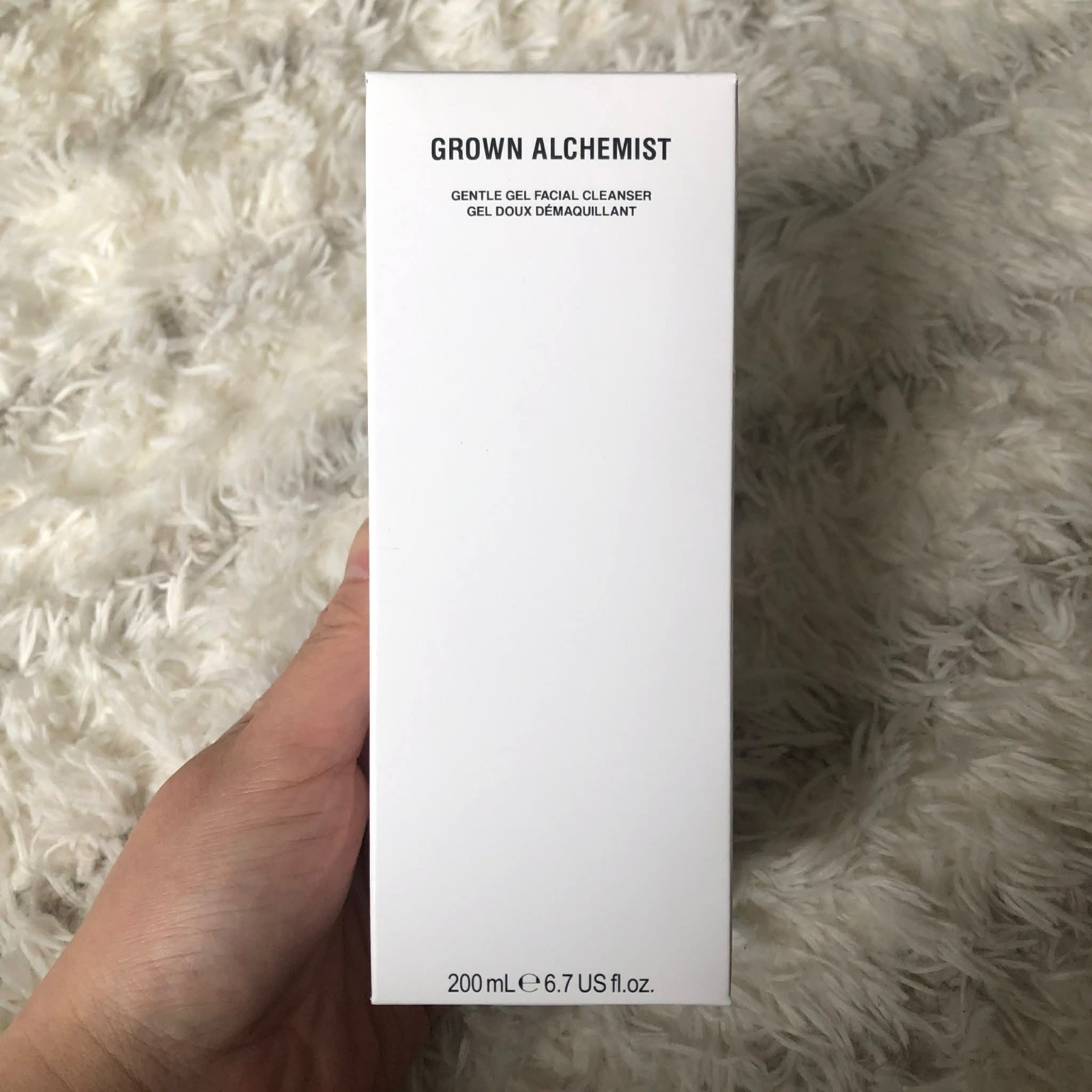 White rectangular box with minimalist design, featuring "GROWN ALCHEMIST" in bold black text, labeled as "Gentle Gel Facial Cleanser," 200 mL size, held against a fluffy background.
