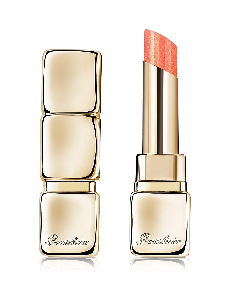 Guerlain KissKiss Bee Glow Pearly Lip Balm features a sleek gold tube with a shiny finish, showcasing a soft peach-colored balm with pearlescent shimmer.